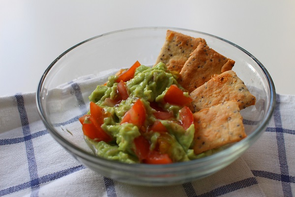 castron transparent in care se afla guacamole cu rosii si biscuiti sarati