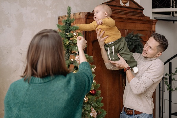 mama care impodobeste bradul, in timp ce tatal a ridicat bebelusul in brate ca sa ajunga la varful bradului