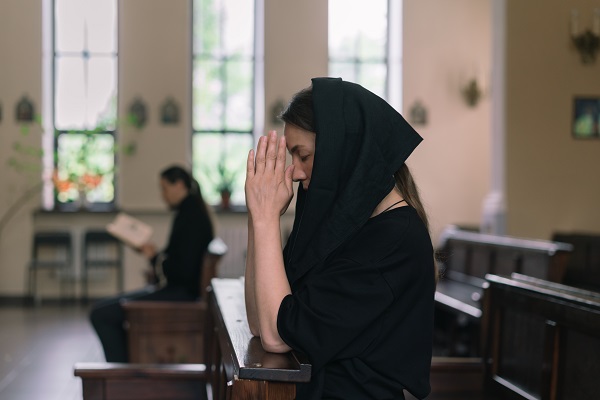 femeie in negru rostind rugaciunea in biserica