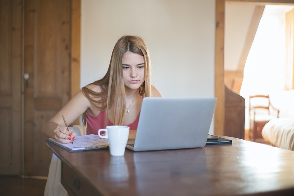 femeie tanara uitandu-se pe laptop si notandu-si apoi diverse lucruri