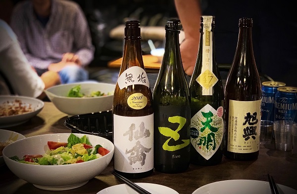 sticle cu diverse sortimente de sake pe o masa, alaturi de diverse salate