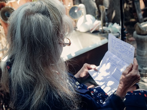femeie in varsta, cu parul lung, grizonat, citind o scrisoare