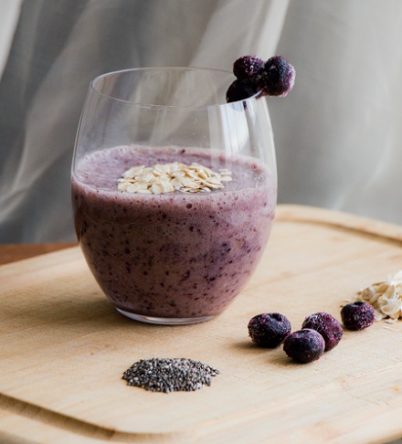 pahar cu smoothie violet, decorat cu fulgi de ovaz si fructe de acai congelate