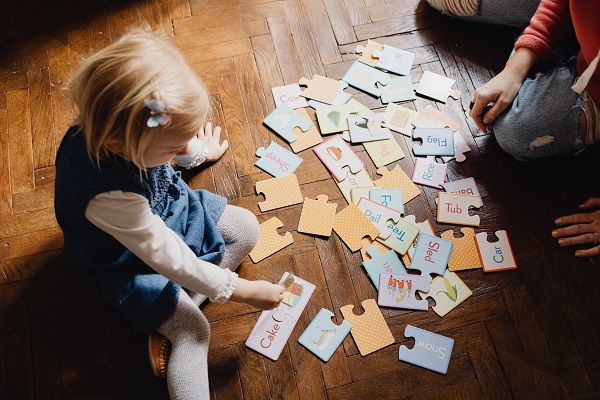 fetita stand pe jos si jucandu-se cu un puzzle alaturi de o femeie