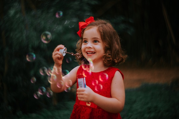 fetita zambitoare in rochita rosie pregatindu-se sa se joace cu baloanele de sapun