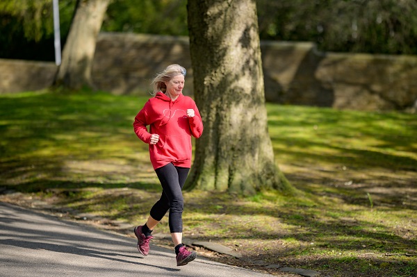 femeie matura in hanorac rosu si colanti negri facand jogging