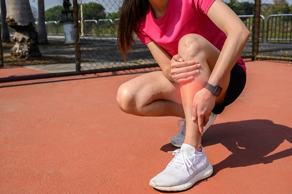 femeie in tinuta sport care isi maseaza piciorul intrucat a suferit o accidentare sau o intindere