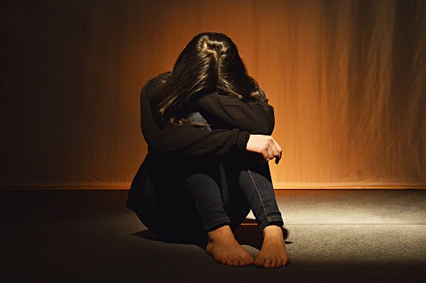 femeie tanara, in pulover negru, desculta, stand jos pe podea si tinandu-si capul pe genunchi