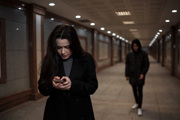 femeie tanara care incearca sa dea un telefon, fiind speriata intrucat crede ca este urmarita de o persoana imbracata in negru