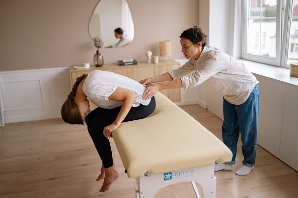 femeie tanara care sta pe o masa de masaj in timp ce terapeutul ei îi face masaj la spate