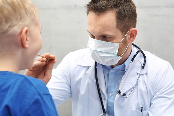 medic care poarta masca de protectie si examineaza gatul unui baietel