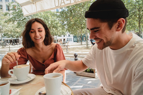 femeie si barbat razand impreuna in timp ce savureaza o cafe la o terasa