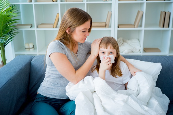 mama care sta pe canapea si incearca sa o aline pe fetita ei, care nu se simte bine si isi sufla nasul