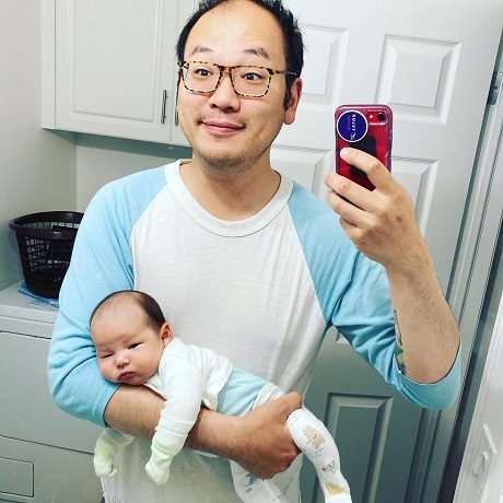 tata de origine asiatica ce isi face selfie in timp ce isi tine in brate bebelusul