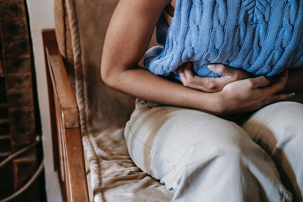femeie care sta pe canapea si pune mainile pe abdomen din cauza durerilor