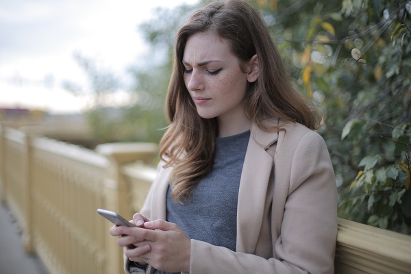 femeie tanara ganditoare uitandu-se pe telefon in timp ce se afla pe terasa