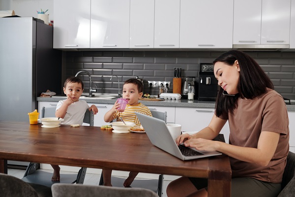 mama lucrand la computer in bucatarie, in timp ce copiii ei stau langa ea la masa