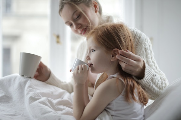 mama care sta alaturi de fetita ei in pat si bea un ceai alaturi de ea