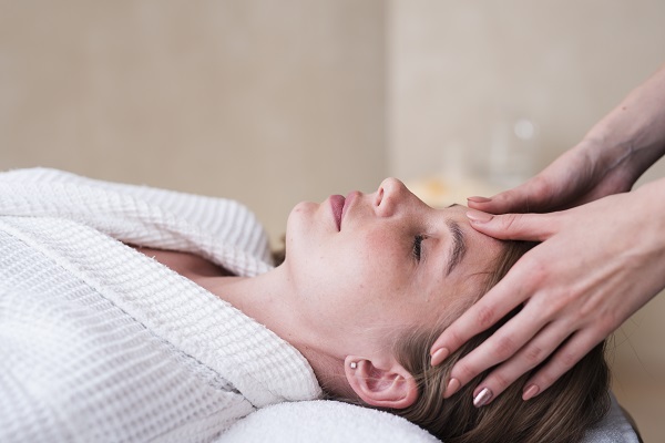 femeie tanara care sta relaxata in timp ce i se face face un masaj facial in zona sinusurilor
