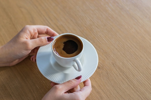 mâini de femeie care tine o ceasca alba de cafea, pe o farfurioara