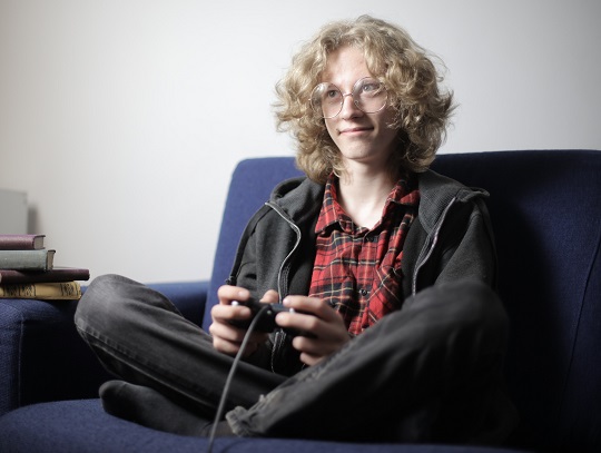 adolescent cu ochelari, care sta pe canapea si se joaca un joc video