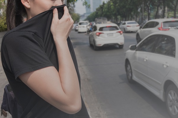 femeie tanara in tricou negru, care incearca sa isi acopere fata pentru a nu inspira esapamentul degajat de masini