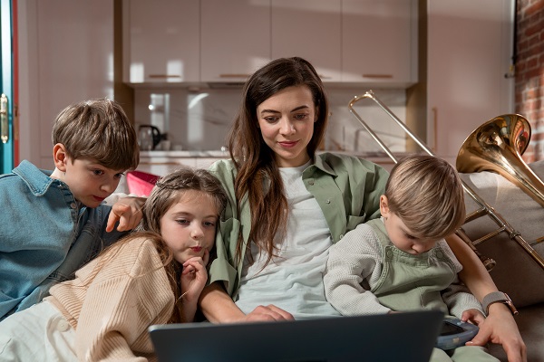 mama cu cei trei copii stand toti pe canapea si uitandu-se pe laptop