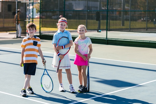 trei copii aflati pe un teren de tenis