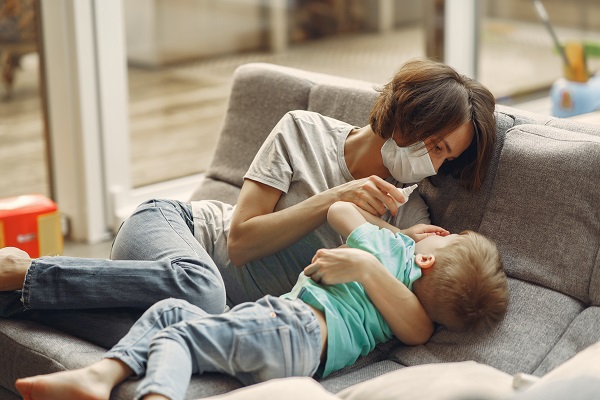 mama ce poarta masca de protectie in timp ce incearca sa-i puna picaturi in nas baietelului ei bolnav