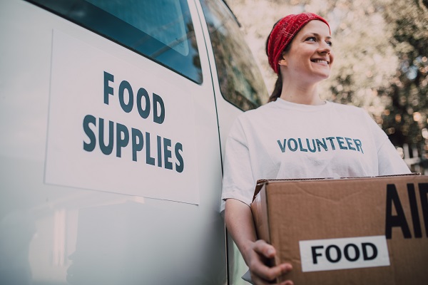 femeie zambitoare ce tine in brate o cutie cu alimente in timpul unei actiuni de voluntariat