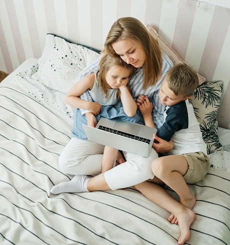 mama care sta pe pat, in fata unui laptopt, alaturi de cei doi copii ai ei