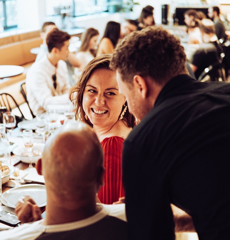 barbat in camasa neagra care sta de vorba cu o femei zambitoare aflata la o masa intr-un restaurant