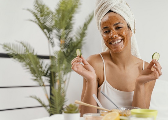 femeie tanara zambitoare, cu un prosop pe cap, ce are pe fata o masca facuta acasa, din ingrediente naturale