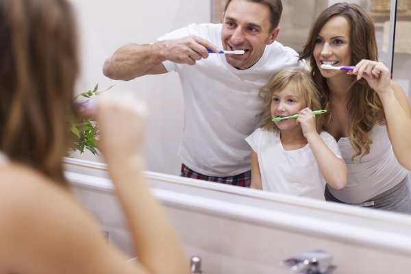 mama, tata si fetita lor spalandu-se toti trei pe dinti, in fata oglinzii din baie