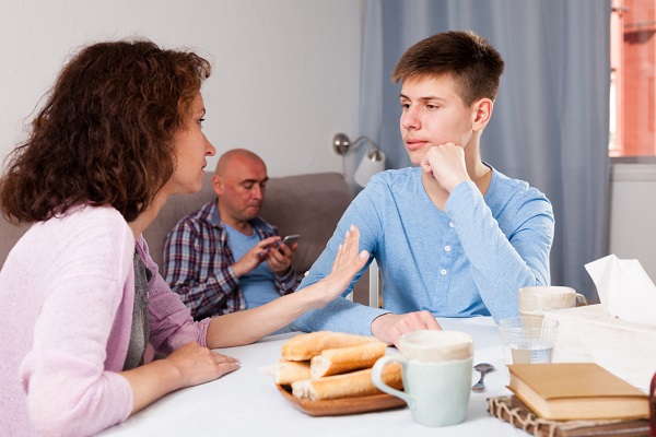 mama care discuta la masa cu fiul ei adolescent, in timp ce sotul ei a ramas pe canapea