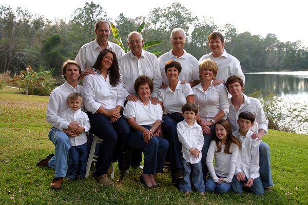 familie numeroasa, purtand camasi albe si blugi, reunita intr-un colt de natura, pe malul unei ape