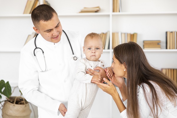 medic care tine un bebelus in brate si mama care incearca sa sarute manuta bebelusului pentru a-l calma