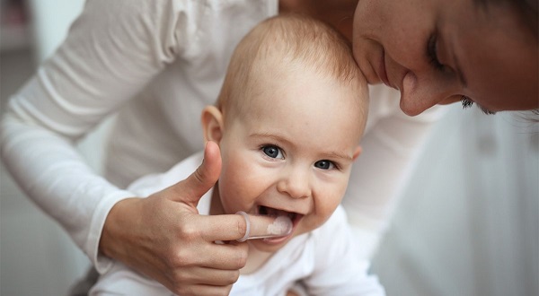 mama care îi face masaj gingival bebelusului ei ajutandu-se de un degetar de silicon