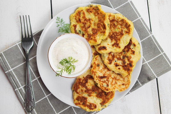 pancakes de legume puse pe o farfurie gri, alaturi de un castronel cu sos alb