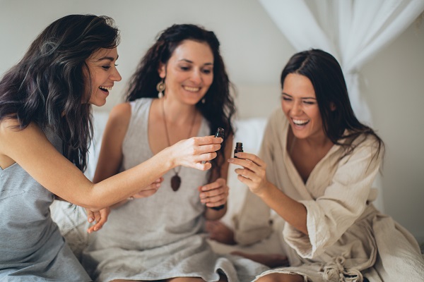 trei femei fericite in tinuta de casa tinand in mâna sticlute cu uleiuri esentiale