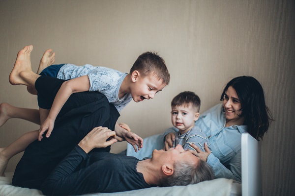 tata care se joaca cu unul dintre baieteii sai, in timp ce mama zambitoare sta langa celalalt baietel