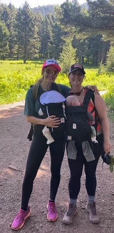 doua femei zambitoare in tinuta sport, ambele tinandu-si bebelusii la piept