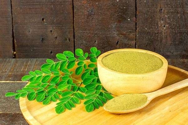 frunze de Moringa, pulbere de frunze de Moringa intr-un castronel de bambus si o lingurita de lemn plină cu pulbere