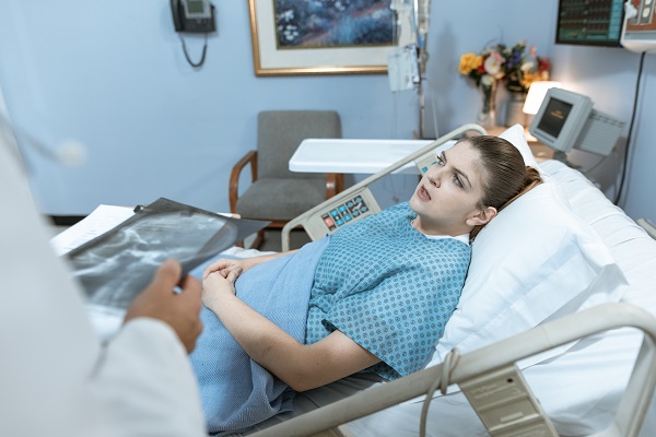 femeie tanara, aflata pe patul de spital, in timp ce un medic sta langa ea si discuta despre rezultatele unei radiografii
