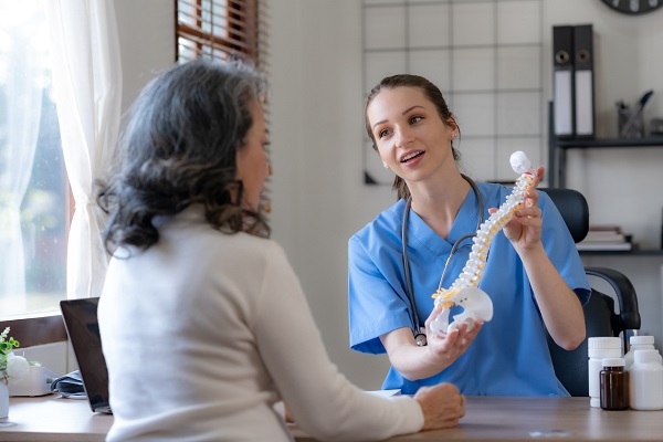 pacienta matura in timpul unei consultatii in cadrul careia doctorita îi da explicatii tinand in mana un mulaj al coloanei vertebrale