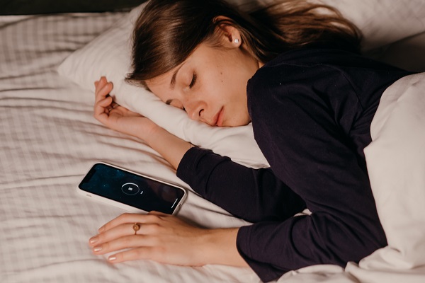femeie tanara in pijama cu maneca lunga de culoare inchisa dormind cu telefonul langa ea