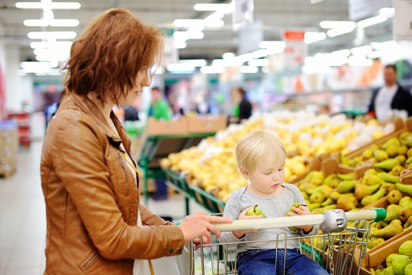 mama la cumparaturi cu baietelul ei, care sta pe cosul de cumparaturi cu doua pere in mâna