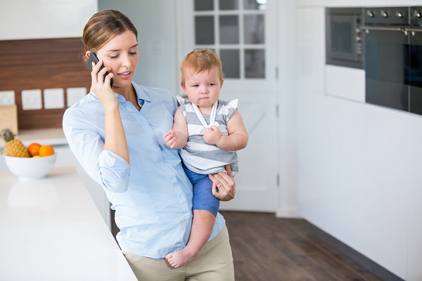 mama care vorbeste la telefon in bucatarie, in timp ce isi tine bebelusul in brate