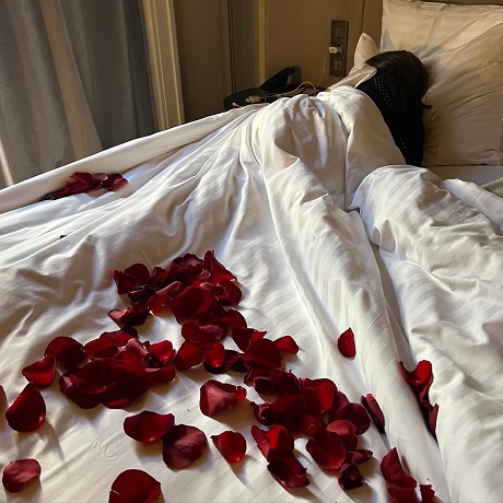 femeie care doarme intr-un pat cu petale de trandafiri rosii