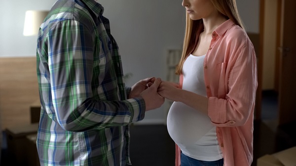 femeie insarcinata si partenerul ei care se tin de mana in timp ce stau unul in fata celuilalt